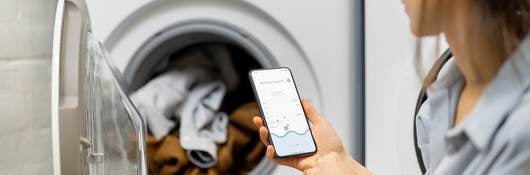 Woman controls washing machine with a smartphone